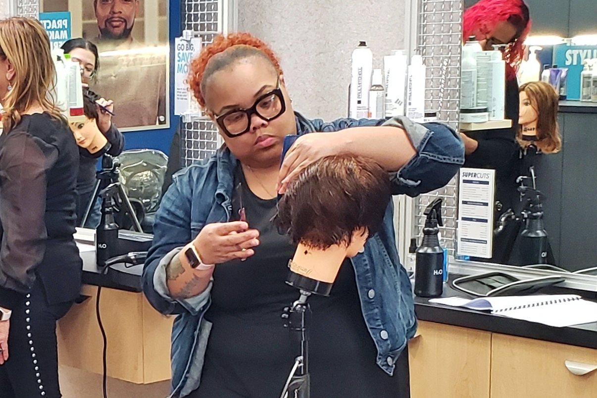 A stylist practicing a haircut on a mannequin head during a training session in one of our salons